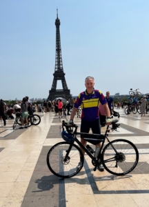 Trustee Steve Hasler stands in the foreground behind his bike, the Eiffel Tower is in the background and the sky is blue